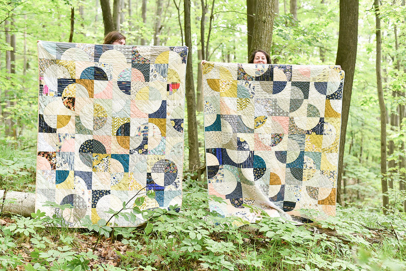 Two people holding up completed Double Time Quilts held up in the forest.